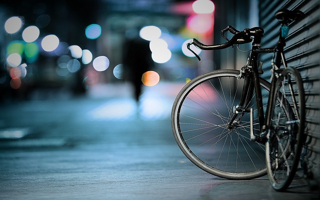 A picture of a bicycle leaning up against a building at night, with the city lights in the background.