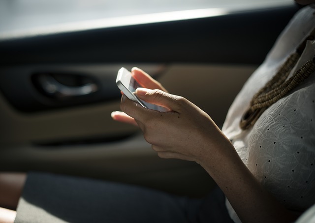 A woman sitting in her car with her cell phone in her hands. She is touching the screen and looking up information.