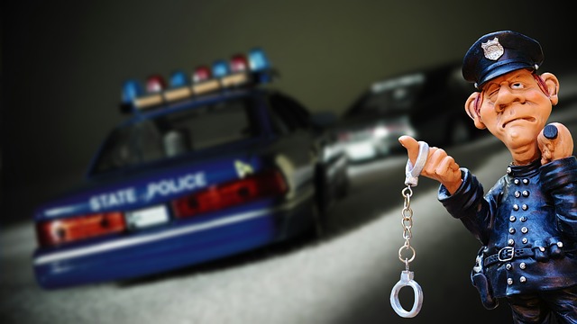 A statue of a police officer holding hand cuffs and standing in front of a police car.